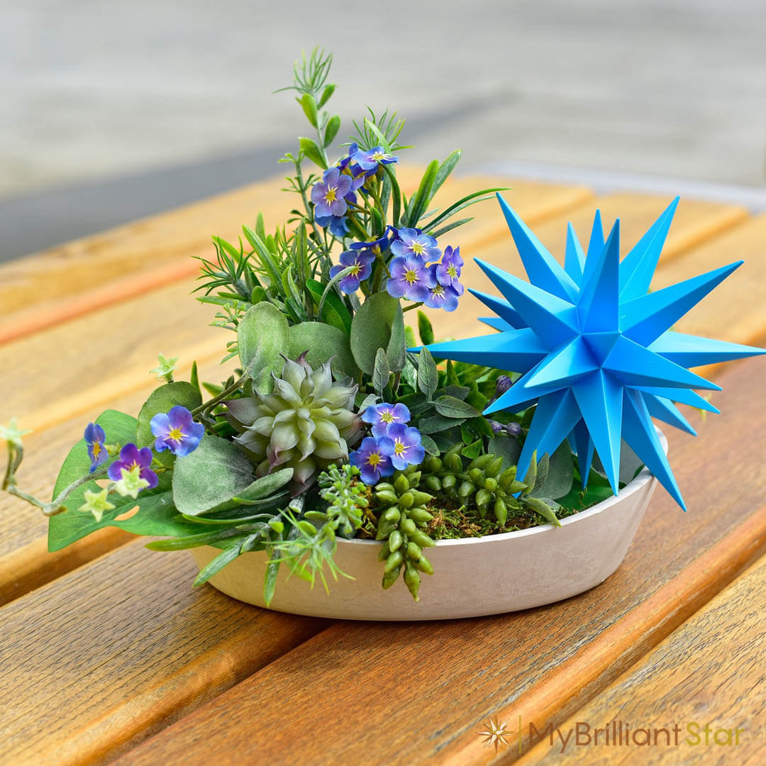 whit shallow vas with green plamnts and purple flowers decorated with the Original Herrnhut plastic star, z-blue, ~ 13 cm / 5 inch ø - LED