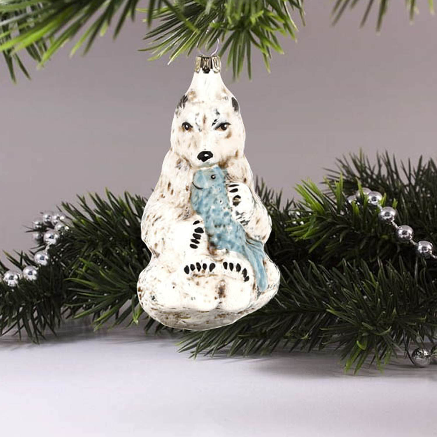 MAROLIN® - Glass ornament "Polar bear with fish" hanging on silver decorated Christmas tree.