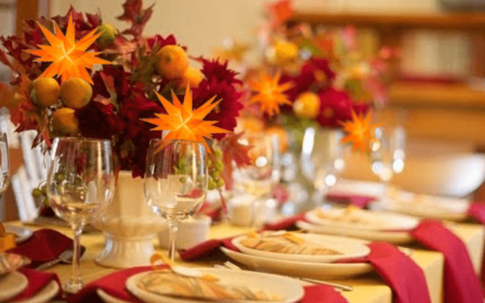 Thanksgiving table set with wine glasses, plates, red napkins, and bouquets with Moravian stars