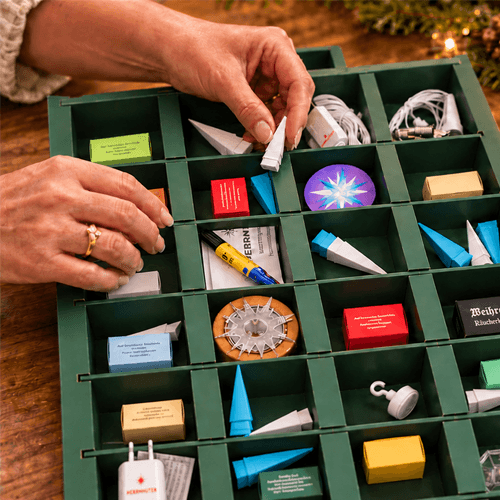 A close-up of a person's hands organizing the items of the Herrnhuter Advent Calendar on a wooden surface.