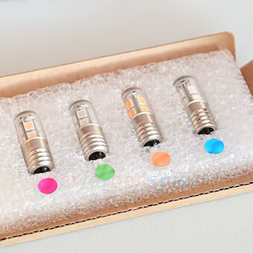 Four small LED light bulbs with clear glass and silver metal bases, arranged in a cardboard tray with bubble wrap. Color circles in pink, green, orange, and blue are placed near each bulb, and a faint watermark is visible across the center.