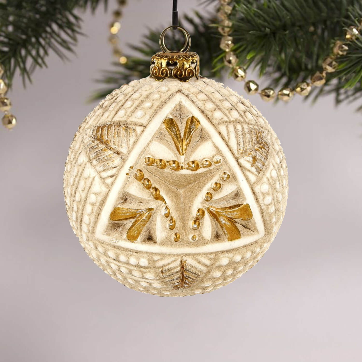 Decorative paper-mâché ball with a textured triangle motive hanging on a tree.