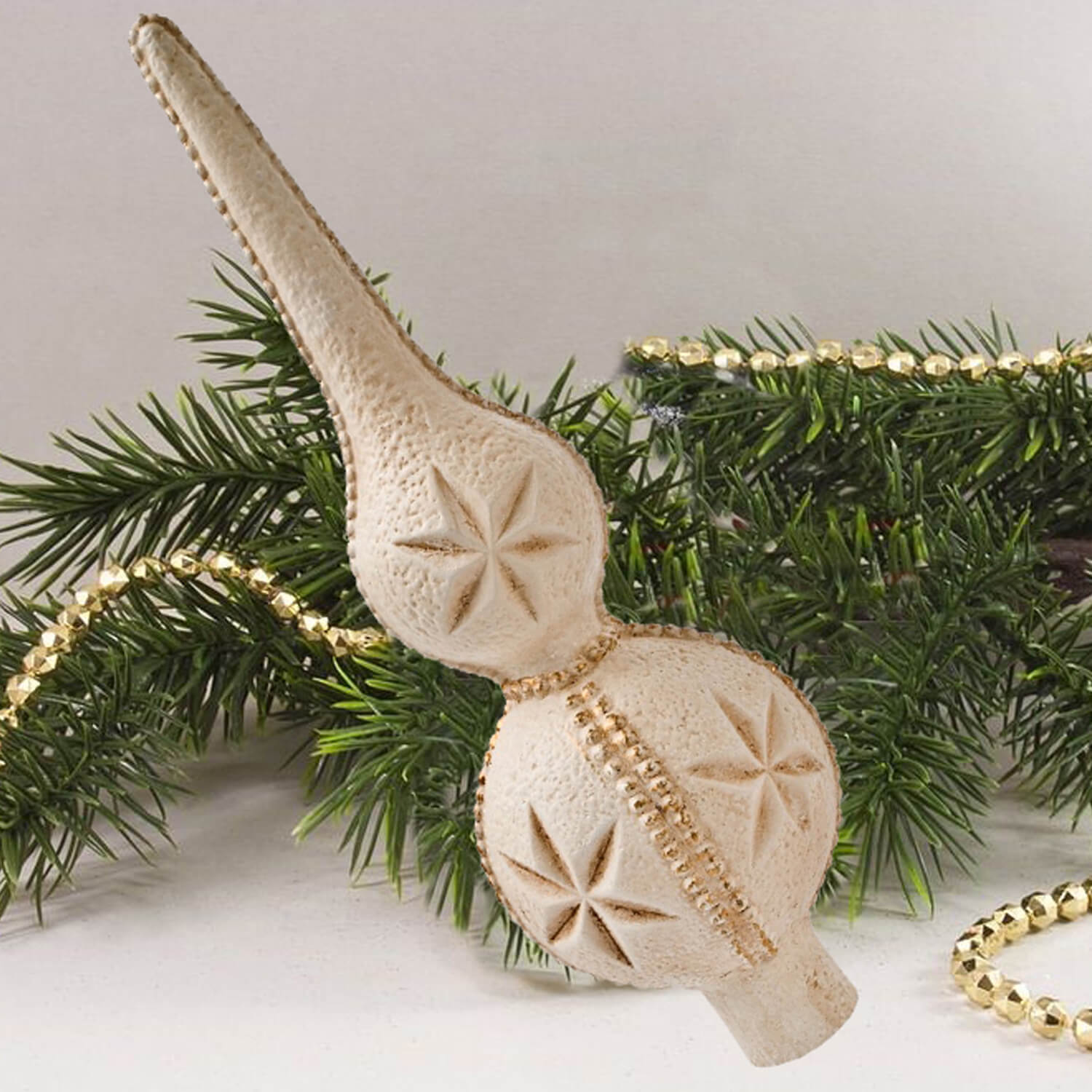 Paper-mâché star tree topper positioned in front of a Christmas tree,  highlighting its antique white finish and subtle gold accents.