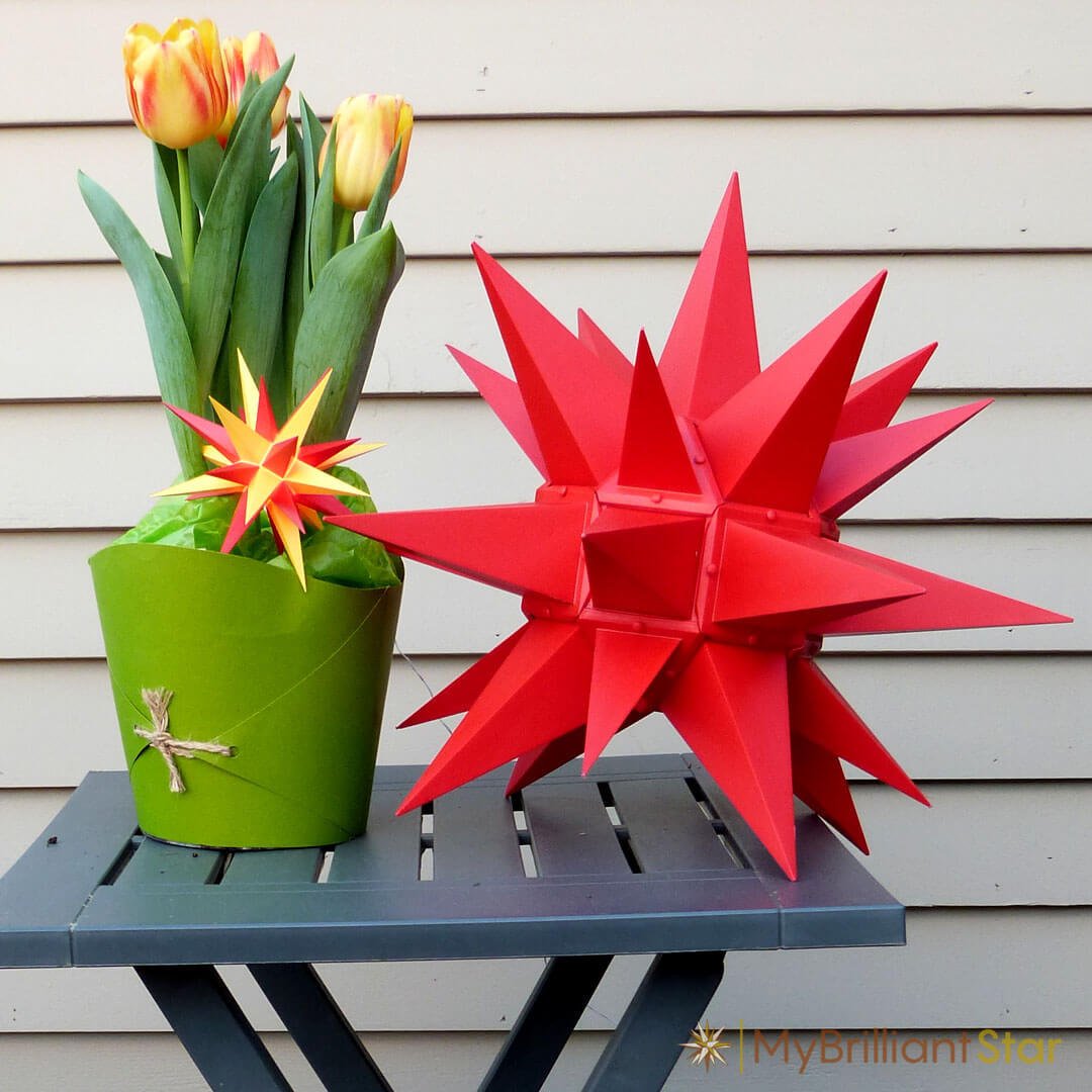yellow and red tulips placed next to Original Herrnhut plastic star, red, ~ 40 cm / 16 inch ø
