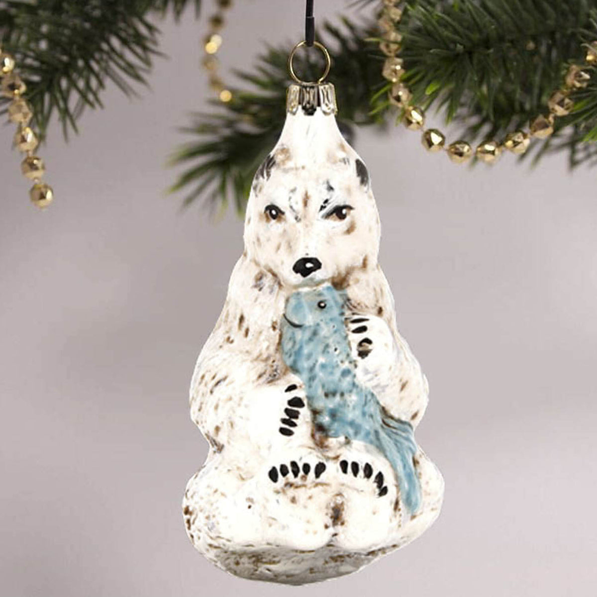 MAROLIN® - Glass ornament &quot;Polar bear with fish&quot; hanging on a golden decorated Christmas tree.