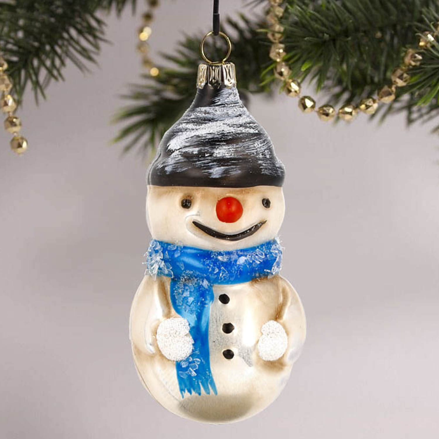 MAROLIN® - Glass ornament "Snowman with scarf and glitter" hanging on a decorated Christmas tree