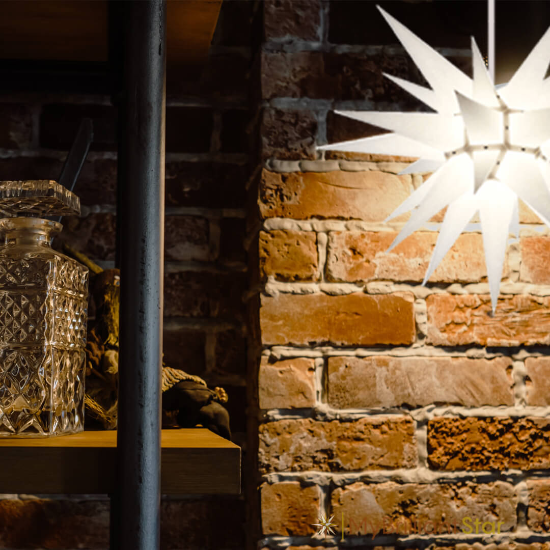Original Herrnhut paper star, white, ~ 60 cm / 24 inch ø hanging in front of a brick wall