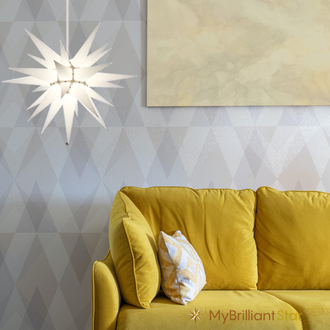 Original Herrnhut paper star, white, ~ 60 cm / 24 inch ø hanging over yellow sofa
