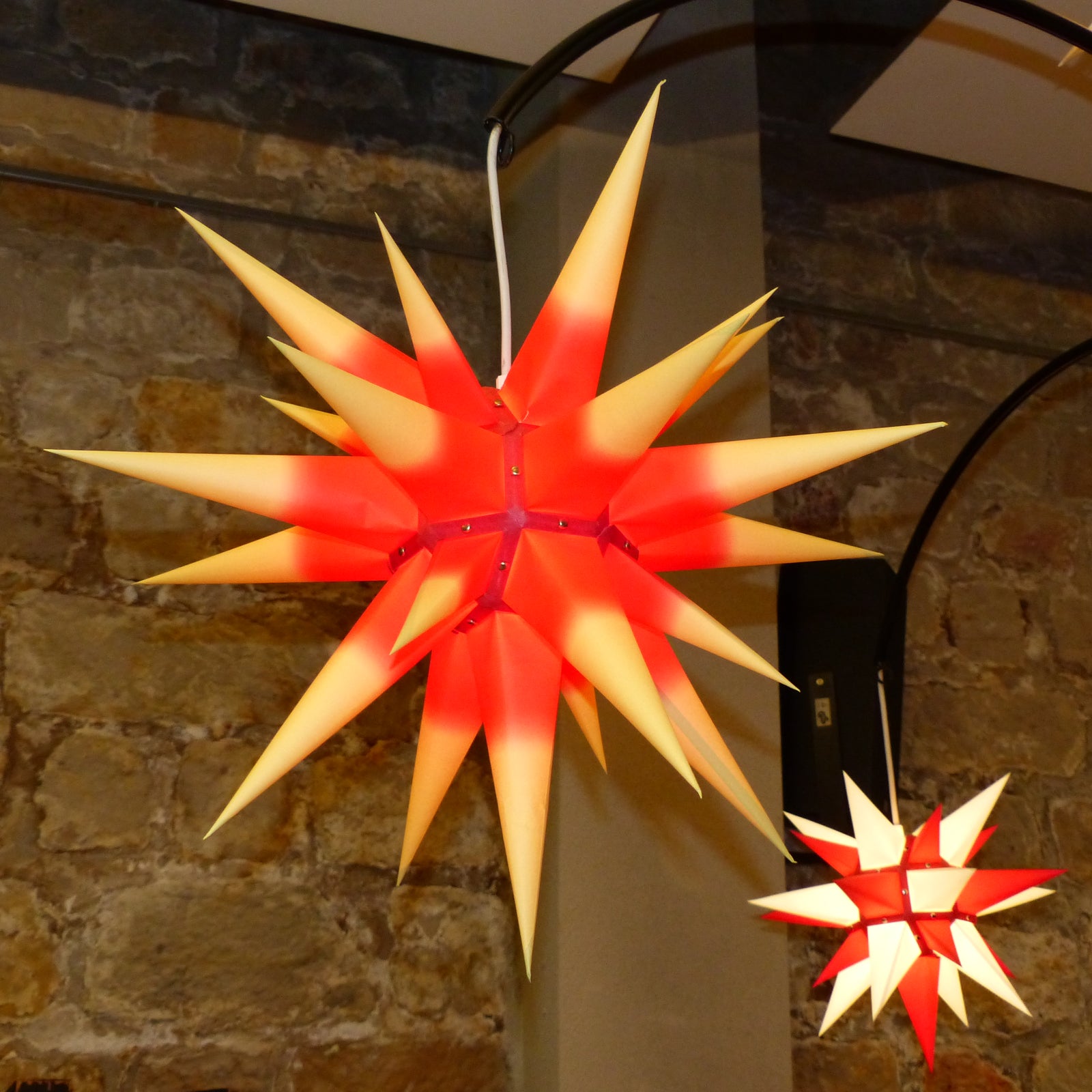 Original Herrnhut paper star, yellow / red center, ~ 70 cm / 27 inch ø hanging next to a smaller herrnhut star in white and red