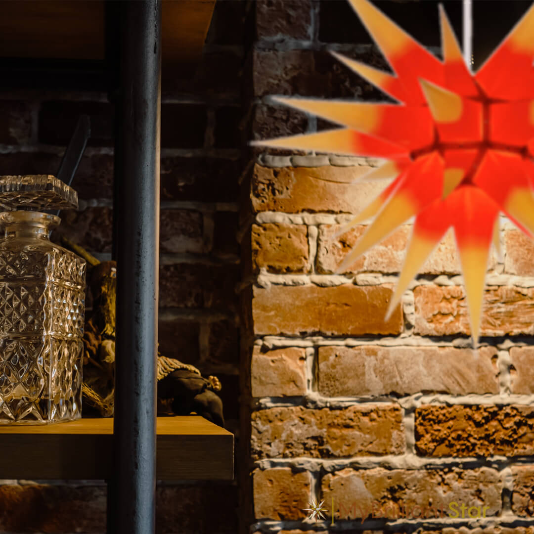 Original Herrnhut paper star, yellow / red center, ~ 70 cm / 27 inch ø hanging in front of a brown wall